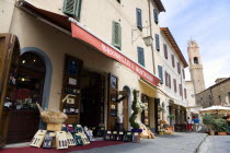 ITALY, Tuscany, Montalcino, Val D'Orcia Brunello di Montalcino Enoteca or wine shop with dispaly of boxed wines on the pavement around its entrance beneath a sunshade. The 14 the Century belltower of...