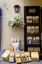 ITALY, Tuscany, Montalcino, Val D'Orcia Brunello di Montalcino Enoteca or wine shop with dispaly of boxed wines on the pavement by its entrance undera potted white gerranium plant beside a wine tastin...