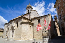ITALY, Tuscany, San Quirico D'Orcia, The Collegiata Church of the saints Quirico and Giulitta. Flags of the Castello Quartieri or quarter of the medieval town decorate the water well in the square bes...