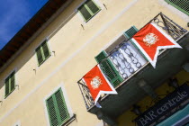 ITALY, Tuscany, San Quirico D'Orcia, Shuttered window facade and balcony of the Bar Centrale in the main square decorated with the red and white banner bearing the crest of the Castello Quartieri or q...