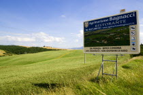 ITALY, Tuscany, Val D'Orcia, Agritourism sign for restaurant in field of ripe crops in the valley near Pienza.
