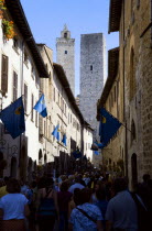 ITALY, Tuscany, San Gimignano, Via di Querececchio lined with flags and busy with tourists walking past shops towards two of the town's medieval towers.