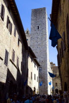 ITALY, Tuscany, San Gimignano, Via di Querececchio lined with flags and busy with tourists walking past shops towards two of the town's medieval towers.