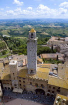 ITALY, Tuscany, San Gimignano, View of the Palazzo Vecchio del Podesta of 1239 with its medieval tower with tourists in the Piazza del Duomo with rooftops and Tuscan farmland on the slopes of the hill...