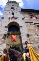 ITALY, Tuscany, San Gimignano, Medieval costumed procession pageant through the streets passing in front of one of the towers in Piazza della Cisterna in the hill town.