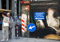 ITALY, Tuscany, Florence, Tourist couple walking past a billboard outside the Uffizi Gallery that conceals renovation work, the man staring open mouthed at the figure in the painting of a woman showin...