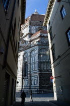 ITALY, Tuscany, Florence, The Dome of the Cathedral of Santa Maria del Fiore the Duomo by Brunelleschi and marble sides of the church seen down a narrow street with people walking past.