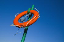 IRELAND, County Dublin, Howth, Red life belt on green stand with blue sky and plane behind. 