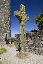 IRELAND, County Louth, Monasterboice Monastic Site, The West Cross is one of the tallest High Crosses in Ireland at 6.5 metres, angular view of east face with Round Tower in the background.  