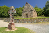 IRELAND, County Wexford, Irish National Heritage Park, Reconstruction of a typical monastic oratory with replica of a celtic cross in front.  
