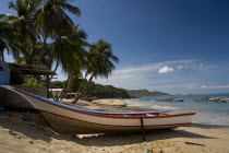 VENEZUELA, Margarita Island, Playa la Galera, Boat on the tropical beach just in front of a small house and palm trees while other boats are noticeable at the crystal clear seawater, shoot on a bright...