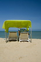 VENEZUELA, Margarita Island, Playa Caribe, View of a green tent at the Playa Caribe beach with a person reading the Margarita Islands map under the shade of the tent, just in front of the exotic seawa...