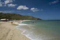 VENEZUELA, Margarita Island, Playa Caribe, View of exotic beach with people swimming and walking on the sand while deck chairs, bars and restaurants are noticeable, shoot on a bright day with blue sky...