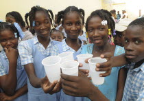 HAITI, Isla de la Laganave, School children holding plastic cups of water from plumbing paid for by Lemon Aid Scottish Charity.