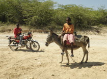 Haiti, Isla de Laganave, Girl sat on donkey with man on motorcycle, both on  dirt road.