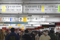 Japan, Tokyo, Shinjuku, inside JR Shinjuku train station, crowd of passengers walking under jumble of train signs, bilingual signs.