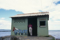 CUBA, West Coast, Vinales,Woman standing in doorway of drinks store building with Vive painted on exterior. The ocean behind.