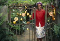 CUBA, Pinar del Rio, Vinales, Elderly woman smiling at gateway to garden hung with pieces of fruit.