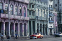 CUBA, Havana, Malecon street scene with crumbling exterior facades of buildings painted pink, blue and green.  Passing cyclists and old cars.  