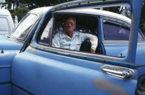 CUBA, Havana, Old Havana, Man in blue car framed by open window.  