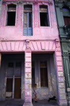 CUBA, Havana, Pink painted crumbling facade of house on the Malecon with girl and dog walking past.