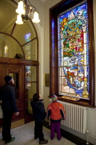 Ireland, North, Belfast, City Hall, Interior,Tourists viewing Centenary Stained Glass Window with various scenes depicted including the construction of Titanic at Harland & Wolf shipyard.