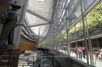 Japan, Tokyo, Yurakucho, the atrium lobby of the International Forum Building, statue of samurai on left, exterior courtyard, trees and flea market, visible through glass wall.