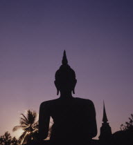 Thailand, Sukhothai, Wat Mahathat, Seated Buddha Statue silhouetted against purple coloured evening sky.