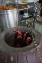 Malaysia, Kuala Lumpur, Skewered Tandoori chicken while being baked inside a Tandoor Oven at the front of an Indian restaurant.
