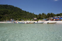 Malaysia, Pulau Perhentian, Terrengganu, Pulau Perhentian Kecil coast with boats shops umbrellas on the beach and a forest in the background.