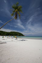 Malaysia, Pulau Perhentian Kecil, Terengganu, Beach scene with a coconut tree and colourful umbrellas and sunbathers.