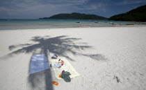 Malaysia, Pulau Perhentian Kecil, Terengganu, Beach scene with towels, sun cream, sunglasses, cigarettes, sandals and book, under the shade of a coconut tree. a