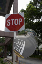 Singapore, stop traffic sign and a curved mirror reflecting the stop letters on the road surrounded by trees.