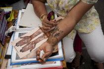 Singapore, Little India, Thieves MArket, Woman painting Henna Tattoo on her own arm whilst leaning on photographs and magazines with tattoo designs.