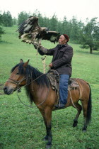 China, Xinjiang Province, Altay Mountains, Kazakh falconer on horseback with eagle used for hunting.