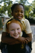 England, West Midlands, Birmingham, Smiling young girls in school playground with the white girl giving her black friend a piggy back. 