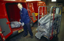 England, East Sussex, Brighton, Male Postal worker unloading sacks of mail from the back of a Post Office red van in the sorting office depot.