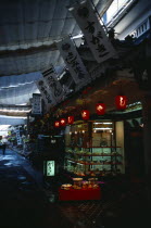 Japan, Honshu, Miyajima, Restaurant with window display and red paper lanterns in street with canopy cover for shade.