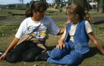 England, East Sussex, Brighton, One teenage girl reassuring another young girl sitting on the grass in Hove Park.