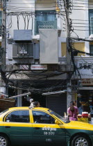 Thailand, Bangkok, Khao San Road, Overhead lectricity cables and transformers above pavement sidewalk with people walking past by and a taxi passing in the street.