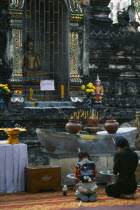 Thailand, North, Chiang Mai, Wat Chettawan Buddhist temple on Tha Phae Road with woman and young girl kneeling and holding incense sticks before a seated statue of Buddha in a niche at an outdoor shri...