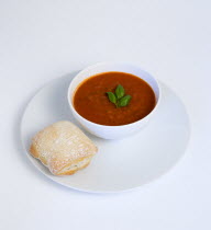 Food, Cooked, Soup, Bowl of tomato and basil soup on a plate with a rustic bread roll on a white background.