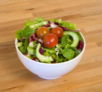 Food, Vegetables, Salad, White bowl of green leaf salad with tomatoes and cucumber on a wooden table top.