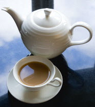 Drink, Hot, Tea, Cup of tea in a cup and saucer beside a teapot on a black granite kitchen worktop with clouds and sky reflected.