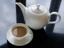 Drink, Hot, Tea, Cup of tea in a cup and saucer beside a teapot on a black granite kitchen worktop with clouds and sky reflected.