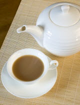 Drink, Hot, Tea, Cup of tea in a cup and saucer beside a teapot on a table with a bamboo mat.