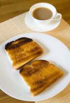 Food, Cooked, Bread, Table setting of two slices of buttered toast on a plate beside a cup of tea in a cup on a saucer.