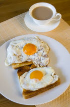 Food, Cooked, Meals, A breakfast table setting of two fried eggs on toast on a plate beside a cup of tea in a saucer.
