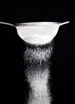 Food, Baking, Flour, White plain flour being siifted through a sieve against a black background.