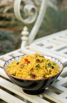 Food, Cooked, Pasta, Bowl of Moroccan couscous with fruit nuts and vegetables on a metal table in a garden.